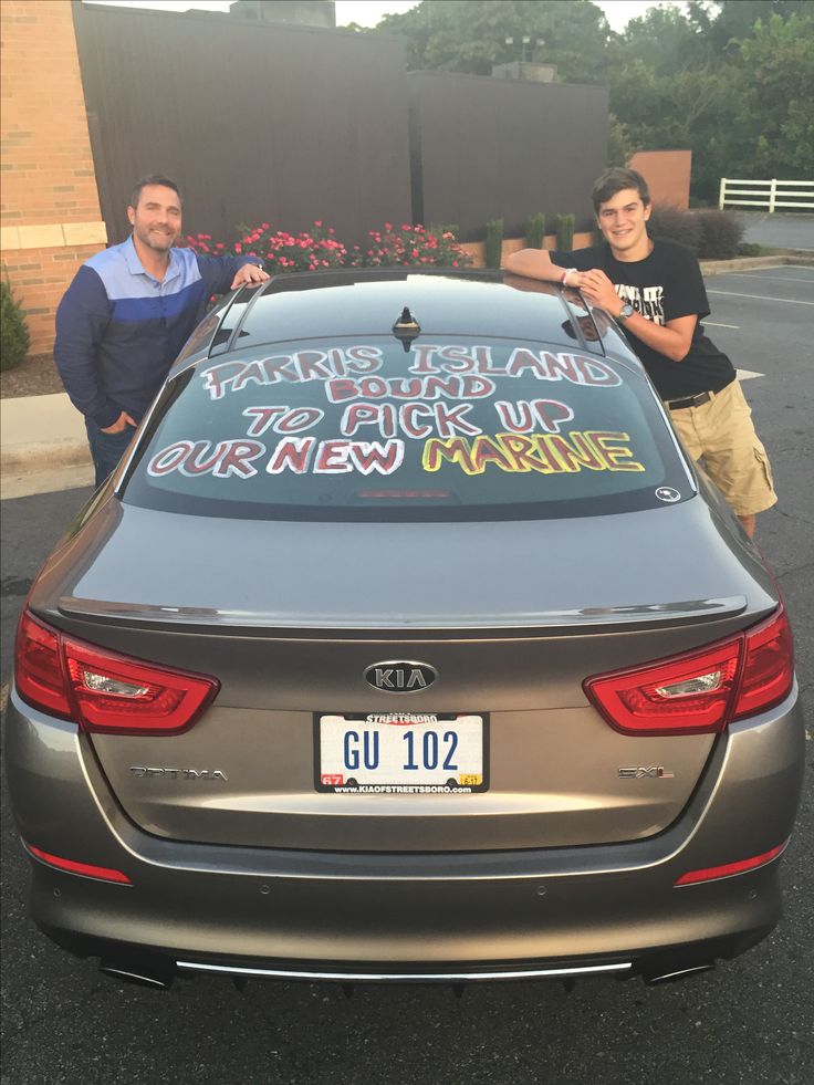 two men standing next to a parked car with signs on the hood and back window