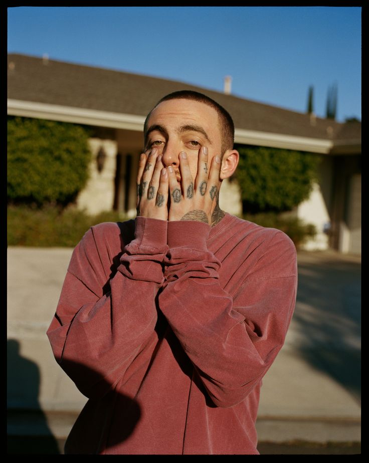 a man covers his face with hands while standing in front of a house on a sunny day