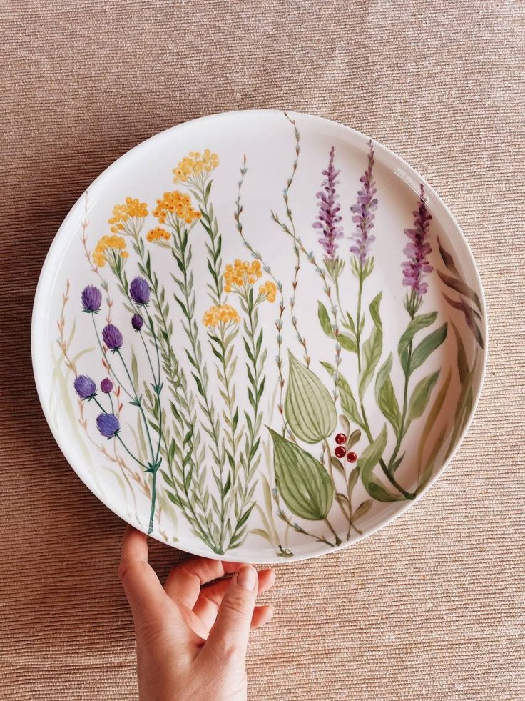 a hand holding a plate with flowers painted on it