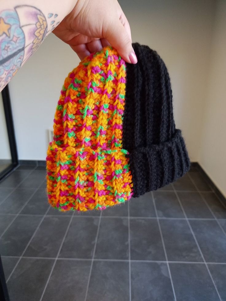 a person holding up a multicolored knitted beanie in front of a tiled floor