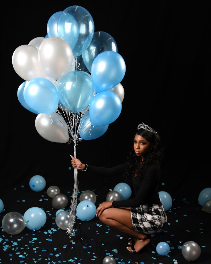 a woman kneeling on the ground holding blue and white balloons