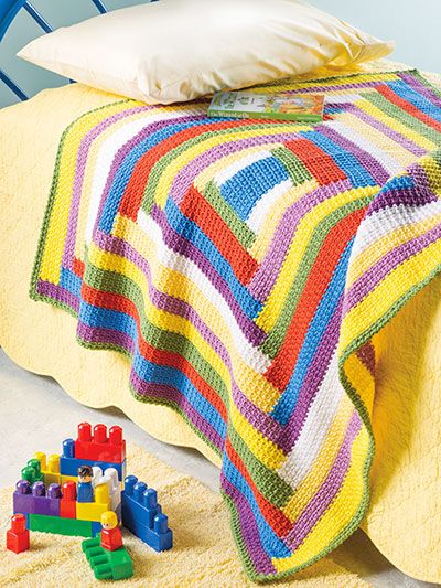 a bed with a colorful blanket on top of it next to a pile of toys