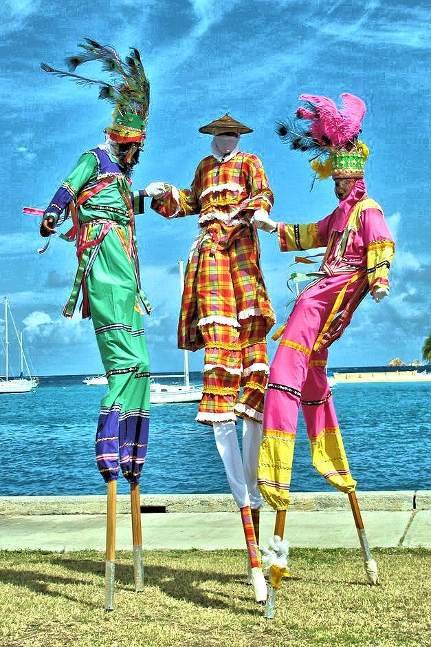 three mannequins dressed in brightly colored clothing stand on stils near the water