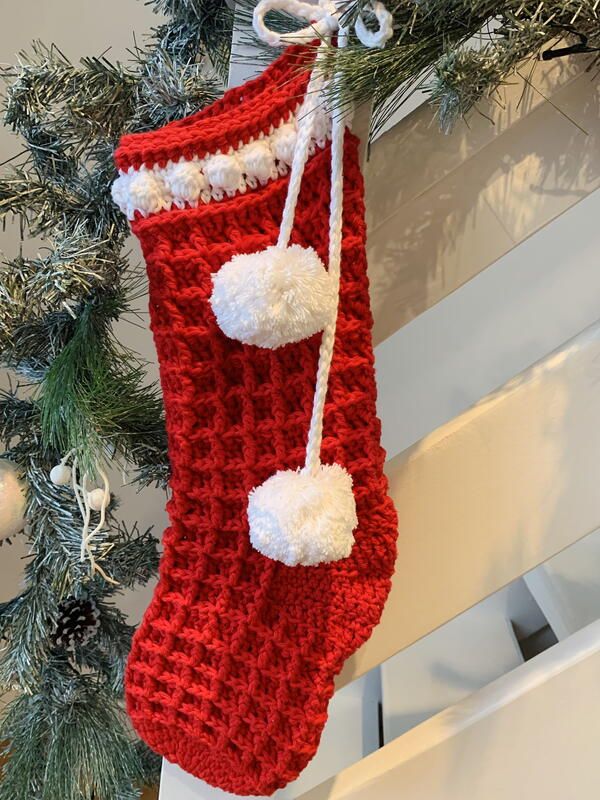 a knitted christmas stocking hanging from a tree with white pom - poms