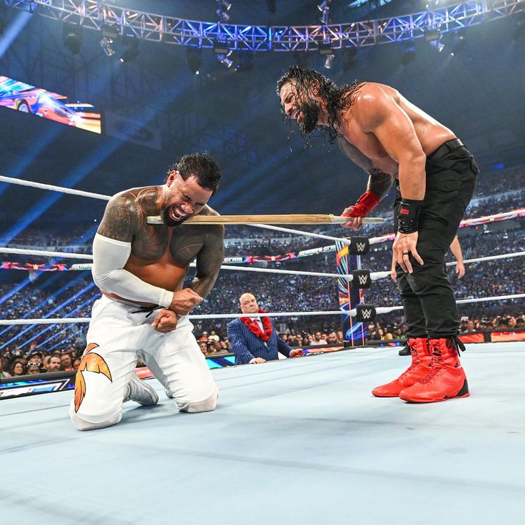 two men in wrestling gear standing next to each other on a wrestling ring with fans watching