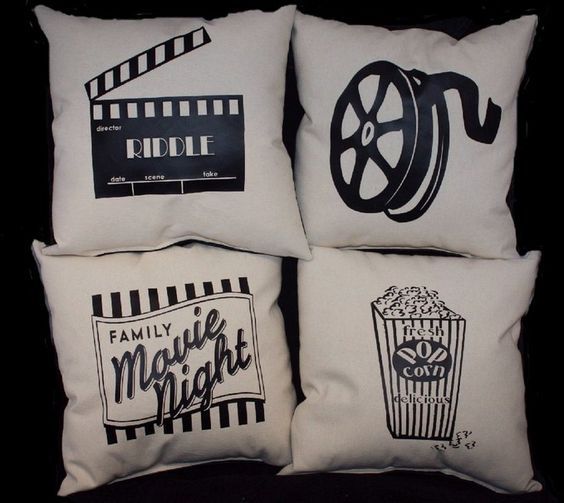 four pillows with movie themed designs are on a black surface and one has a popcorn bucket, the other is a film reel