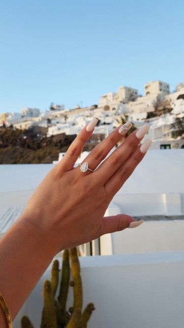 a woman's hand with two rings on her fingers and some cacti in the background