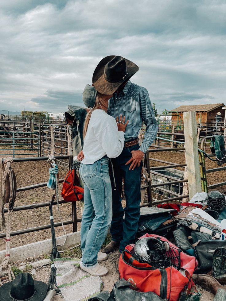 two people standing next to each other in front of a fence with hats on it