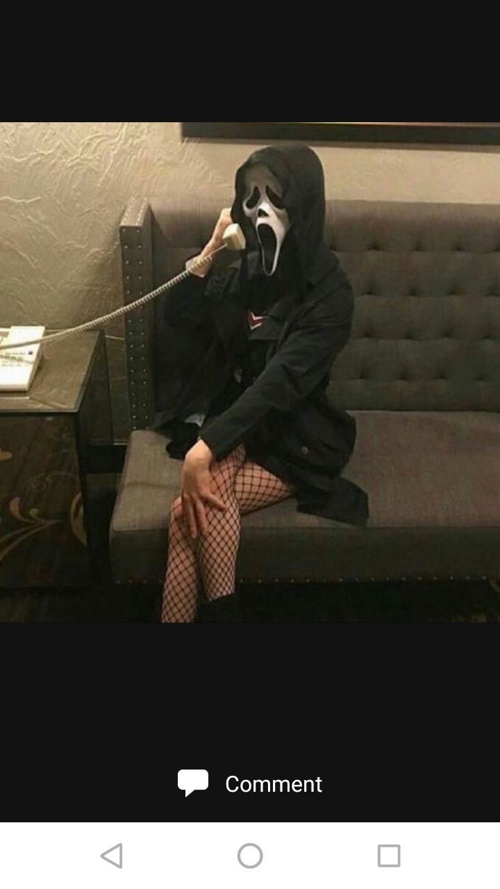 a person in a mask sitting on a couch talking on a cell phone and holding a cord