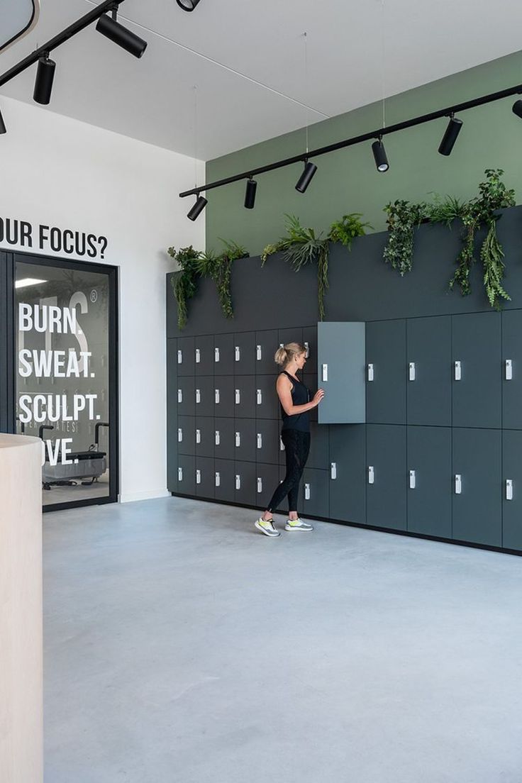 a woman standing in front of a locker with plants on the wall next to it