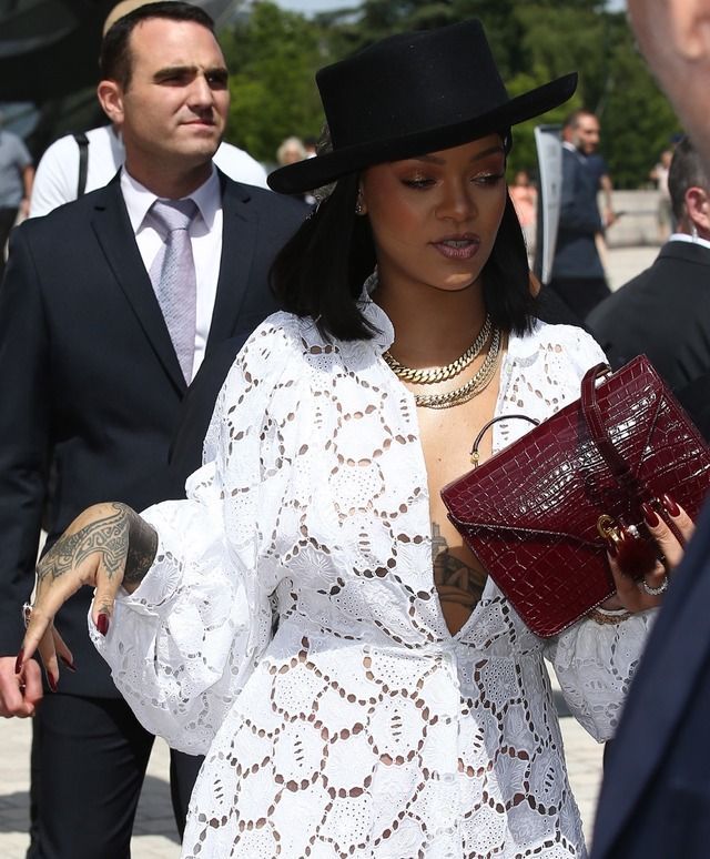 a woman in a white dress and black hat is holding a red purse while another man looks on