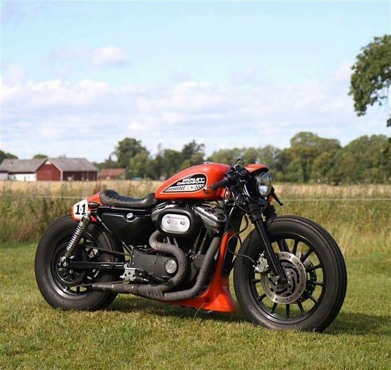 a red motorcycle parked on top of a lush green field next to a tree filled field