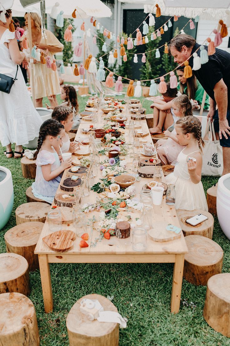 a group of children sitting around a wooden table with food on it and bunting