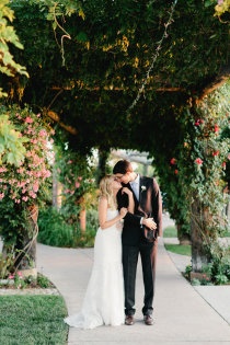 a bride and groom kissing in front of an archway with pink flowers on the side