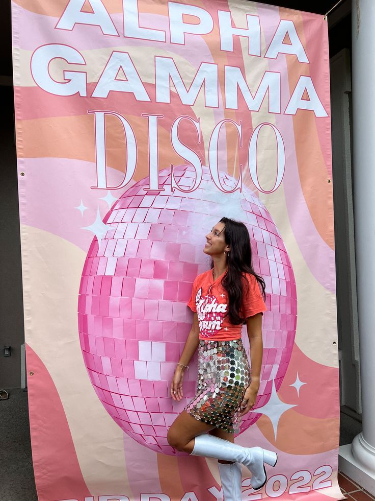 a woman standing next to a pink disco ball on top of a white bike in front of a sign