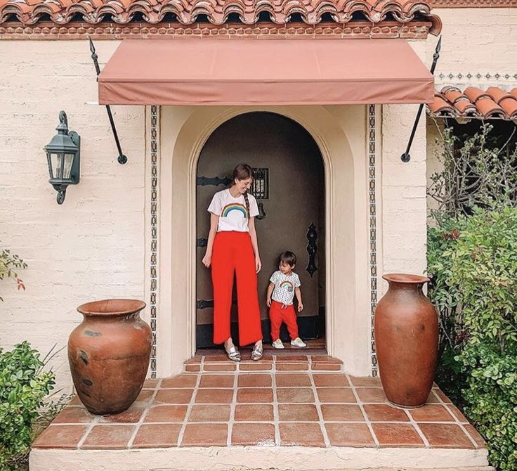 a woman and child standing in front of a doorway with pots on the ground next to them