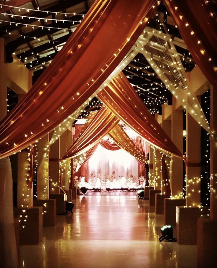 an indoor wedding venue with red and white draping, string lights and fairy lights on the ceiling