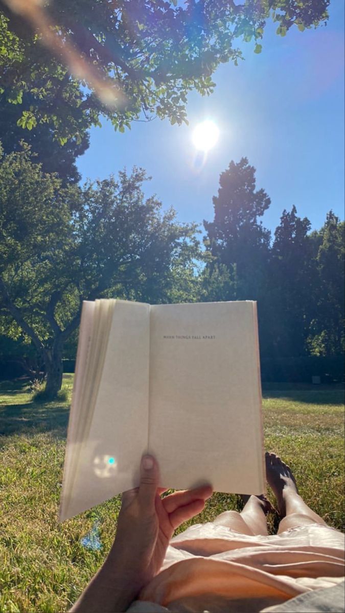 a person laying down reading a book in the grass under a tree with the sun shining on them