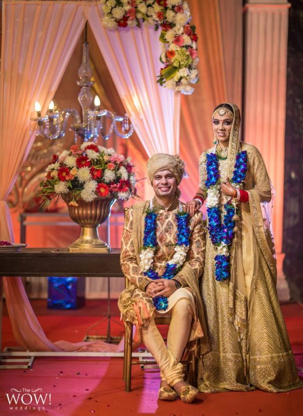 two people sitting on a chair in front of a table with flowers and garlands