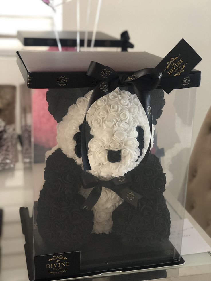 a stuffed panda bear in a black and white box with flowers on it's head