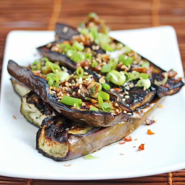 a white plate topped with grilled eggplant covered in sesame seeds and seasoning