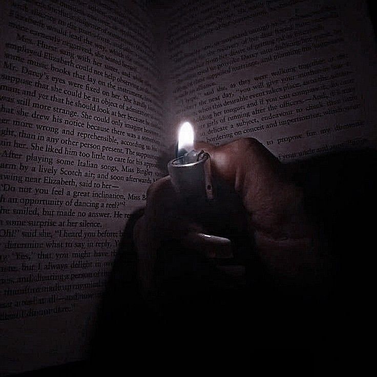 a person holding a lighter in their hand while reading a book with the light on