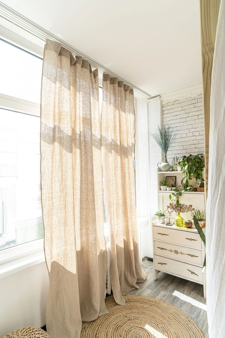 a living room with white brick walls and wooden flooring, beige drapes on the windows