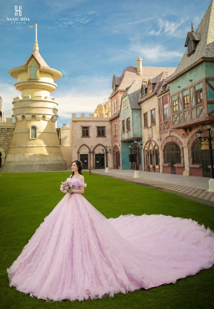 a woman in a pink ball gown standing on the grass near a castle like building