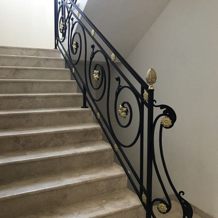 an iron stair railing with gold decorations on the top and bottom handrails in a white room