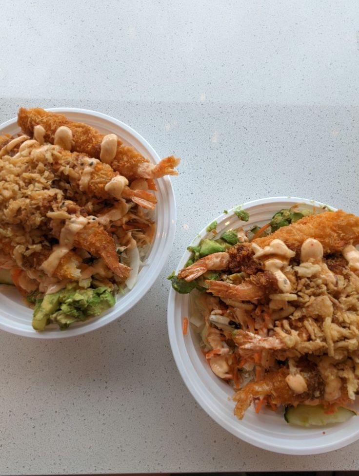 two paper plates filled with food on top of a white countertop next to each other