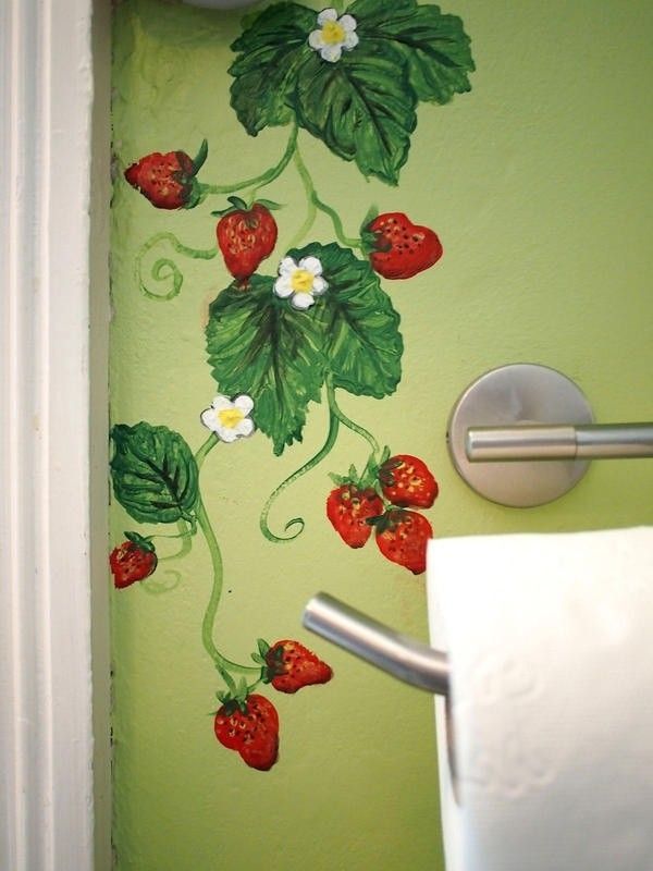 a green wall with strawberries painted on it and a toilet paper dispenser