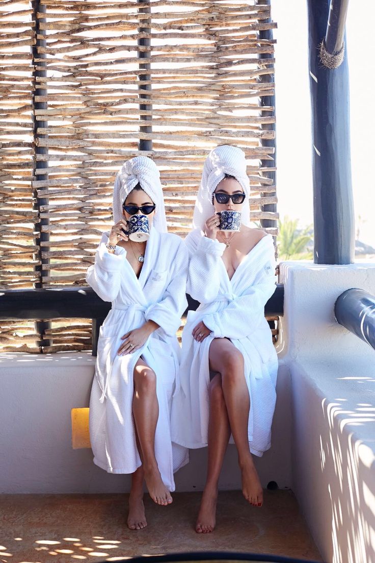 two women in white robes sitting next to each other with their faces covered by towels