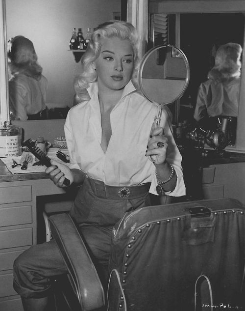 a woman sitting in front of a mirror holding a magnifying glass over her shoulder