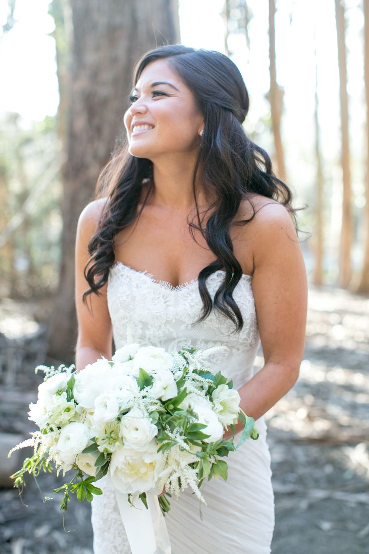 a woman in a wedding dress holding a bouquet and smiling at the camera with trees behind her