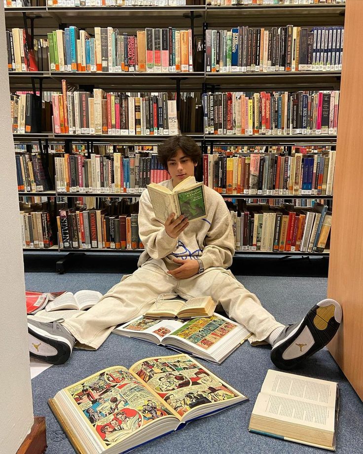 a boy sitting on the floor reading a book in front of a library full of books