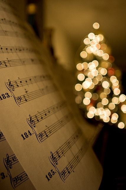 a sheet with musical notes on it and a christmas tree in the background, all lit up