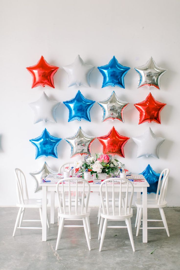 a white table topped with red, white and blue stars next to a wall filled with balloons