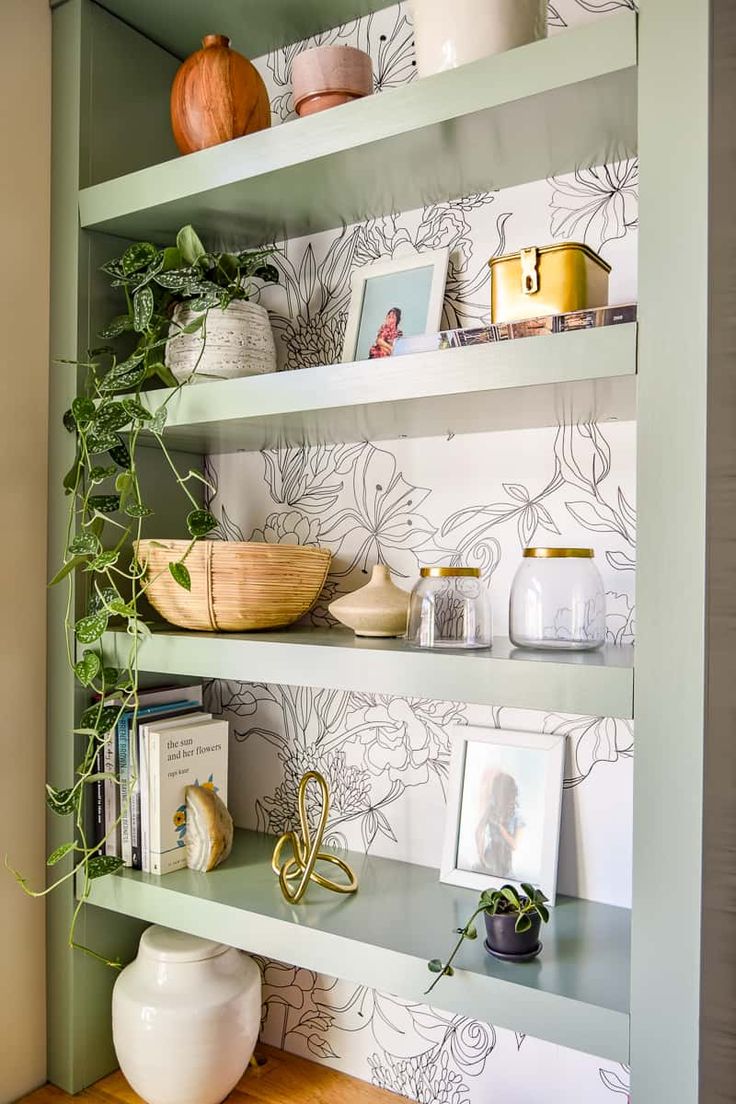 a shelf with some plants and pictures on it in a room that is painted green