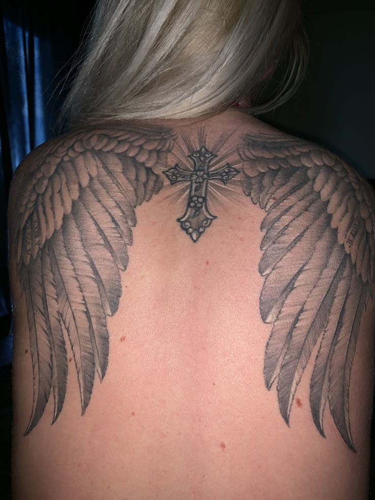 the back of a woman's shoulder with angel wings and a cross on it