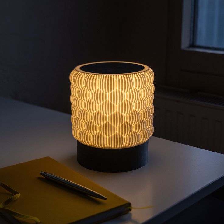 a lamp sitting on top of a table next to a notepad and pen in front of a window