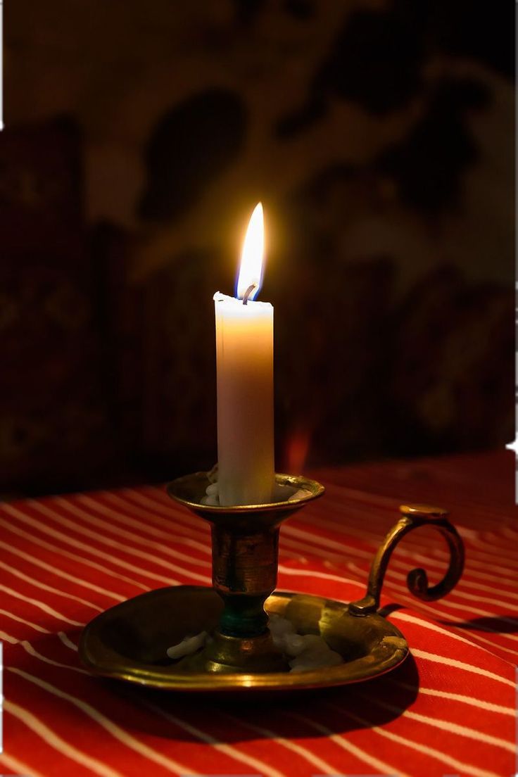 a lit candle sitting on top of a golden plate with a red and white table cloth