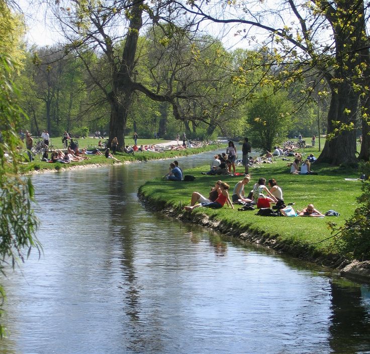 people are sitting on the bank of a river while others sit in the grass by the water