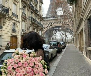 a woman is holding flowers in front of the eiffel tower, with cars parked near her