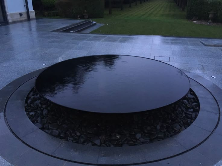 a large black circular fountain in the middle of a patio with water running through it