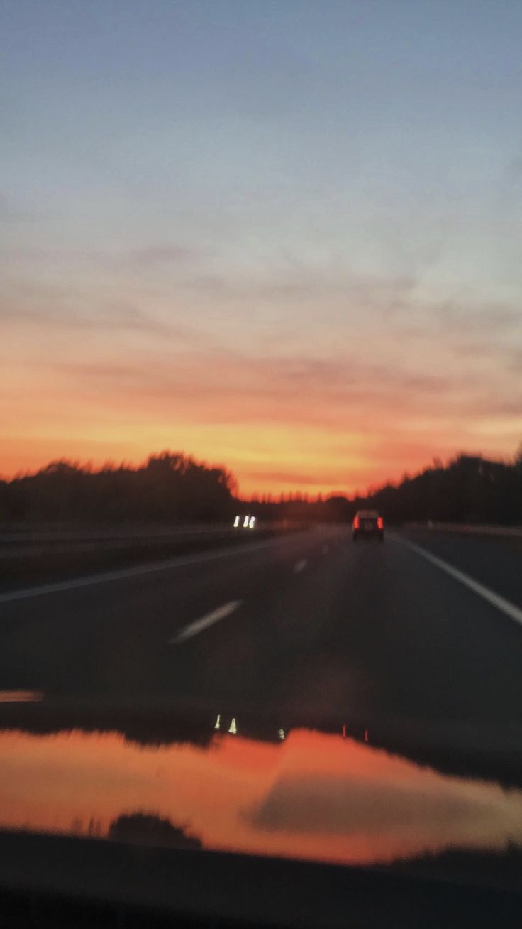 the sun is setting on an empty highway with water puddles in front of it