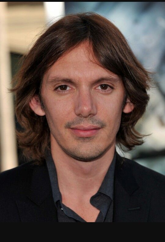 a close up of a person wearing a suit and tie with long hair in front of a movie poster