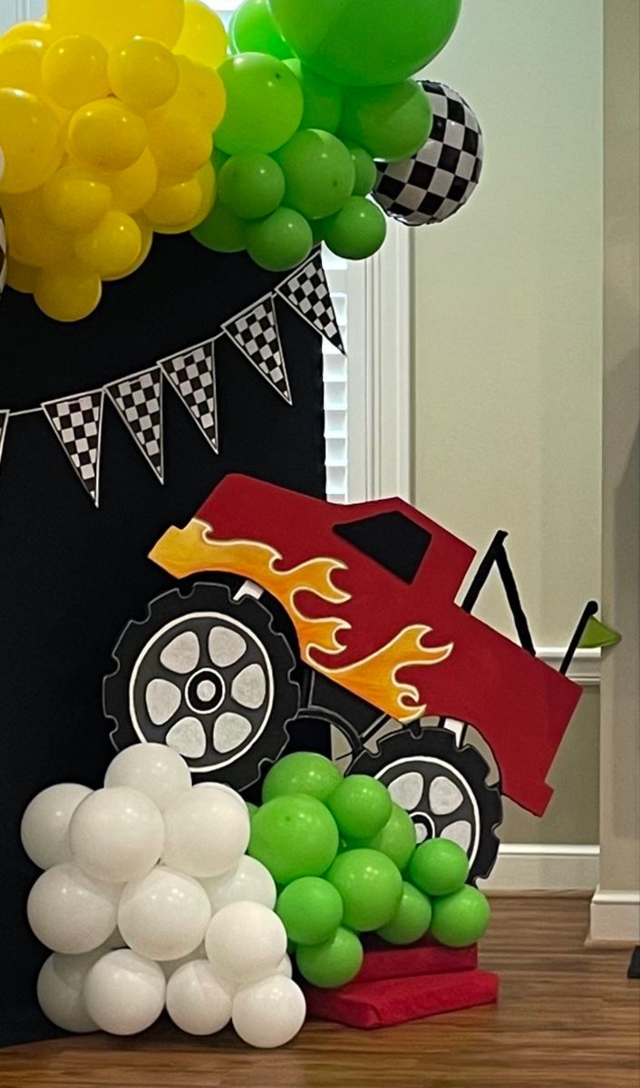 a birthday decoration with balloons and cars on the table in front of a cake topper