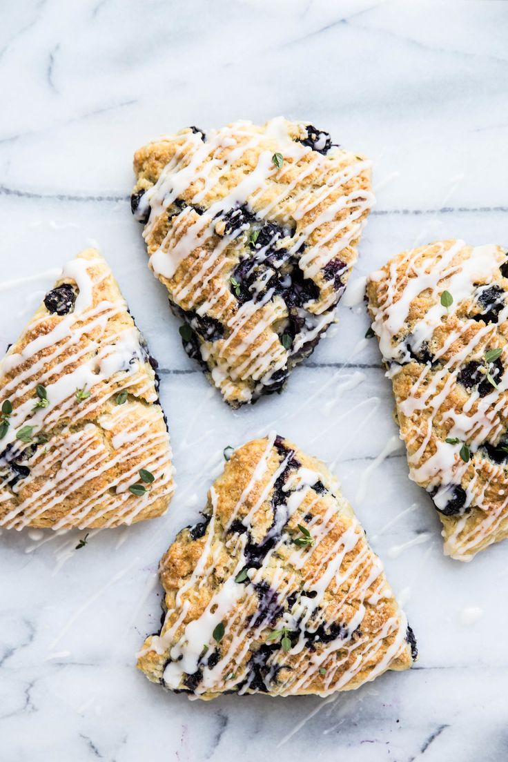 four pieces of blueberry scones on a marble counter top with icing and sprinkles