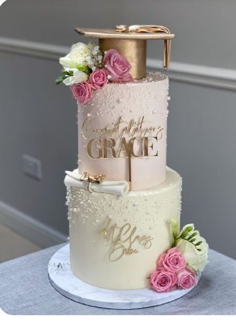 a three tiered cake with pink and white flowers on the side, topped with a gold graduation cap