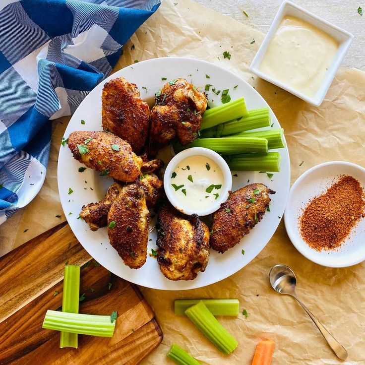 chicken wings and celery on a white plate with ranch dressing in small bowls